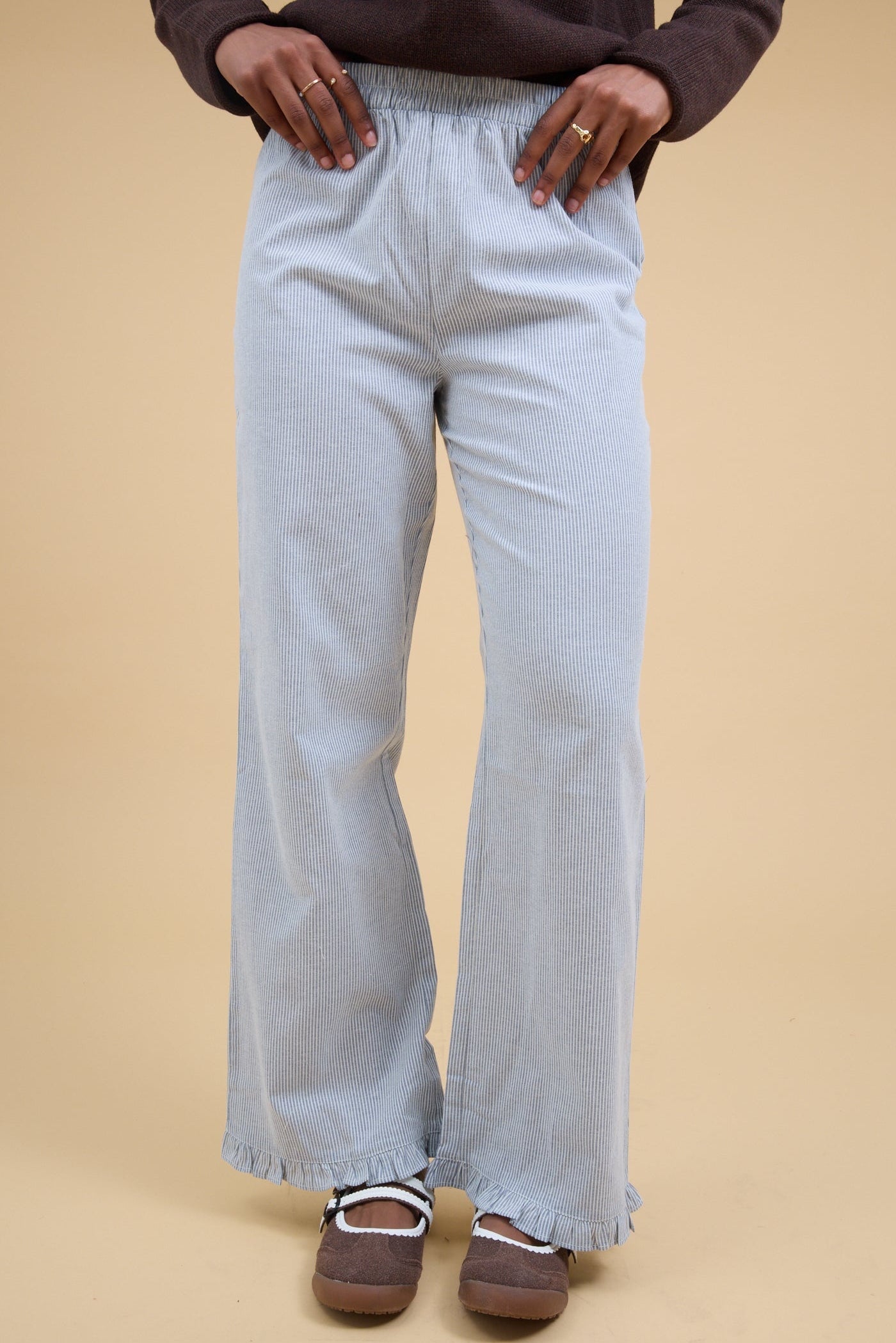 Young woman wearing a pair of navy & white stripe, loose fitting pant with a narrow ruffle hem.