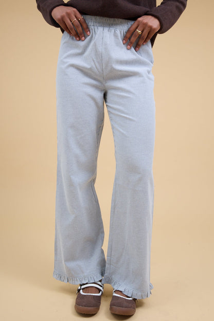Young woman wearing a pair of navy & white stripe, loose fitting pant with a narrow ruffle hem.