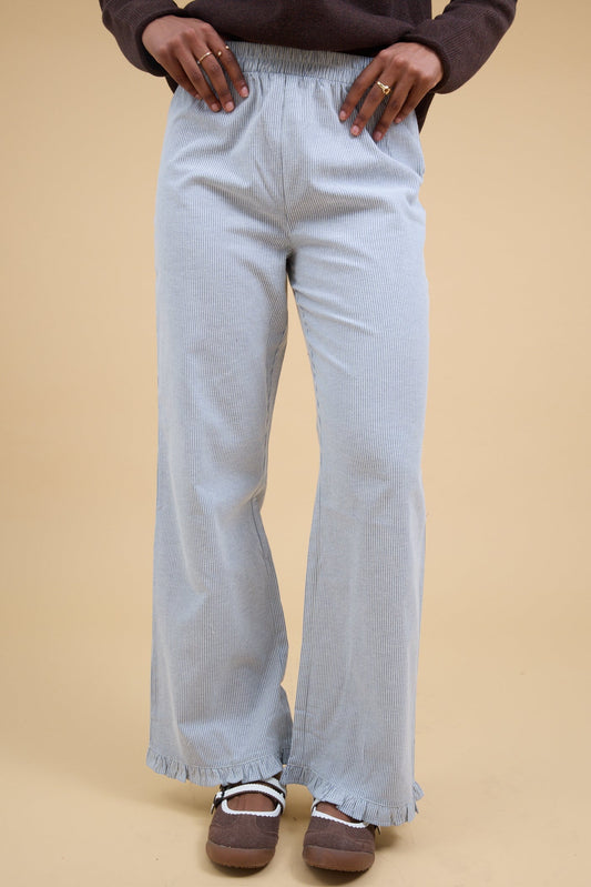 Young woman wearing a pair of navy & white stripe, loose fitting pant with a narrow ruffle hem.