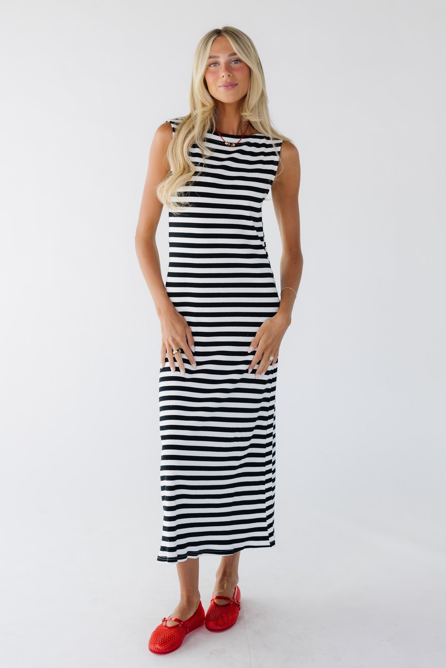 Woman wearing a sleeveless, close fitting rib knit midi dress in black & white stripe.