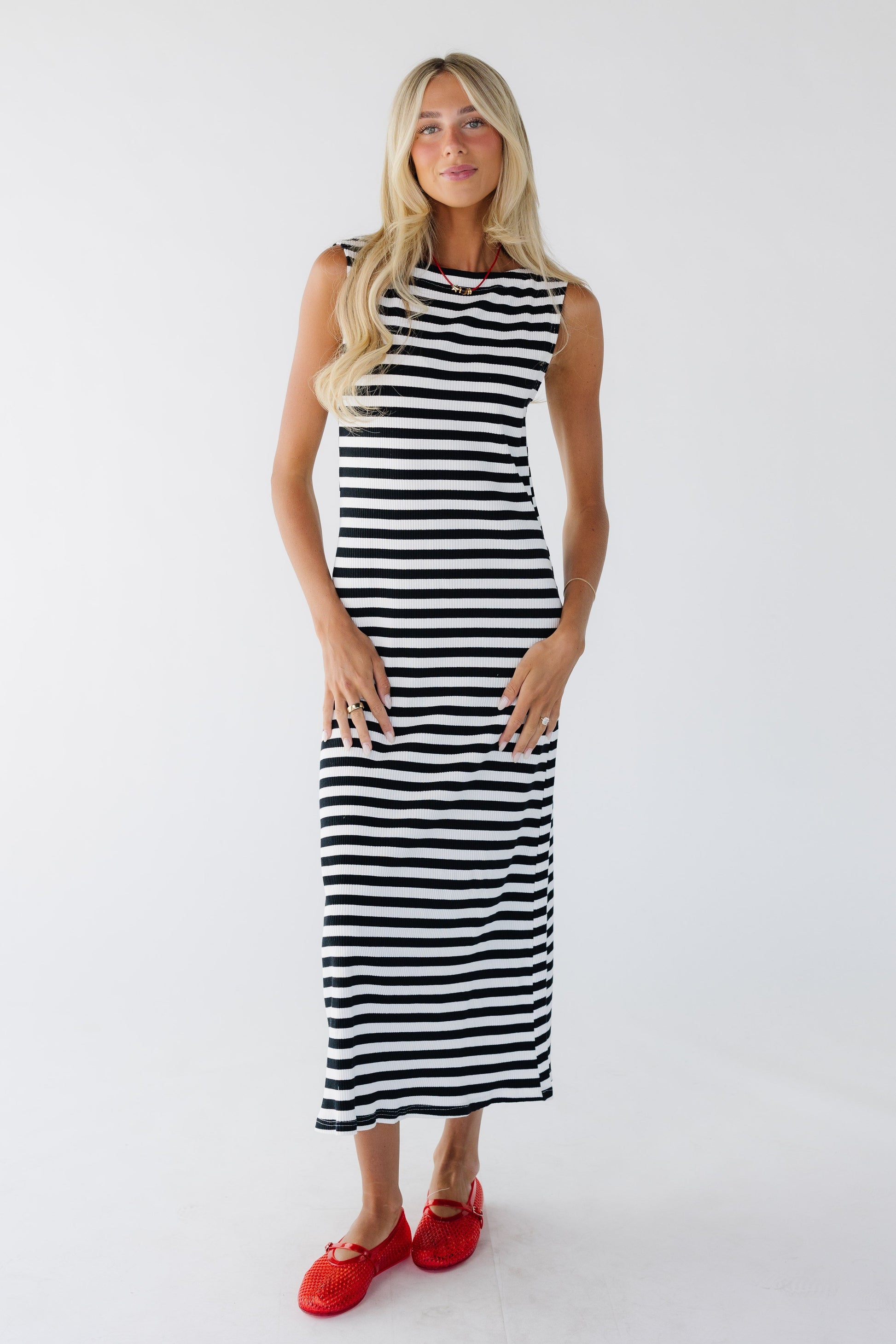 Woman wearing a sleeveless, close fitting rib knit midi dress in black & white stripe.