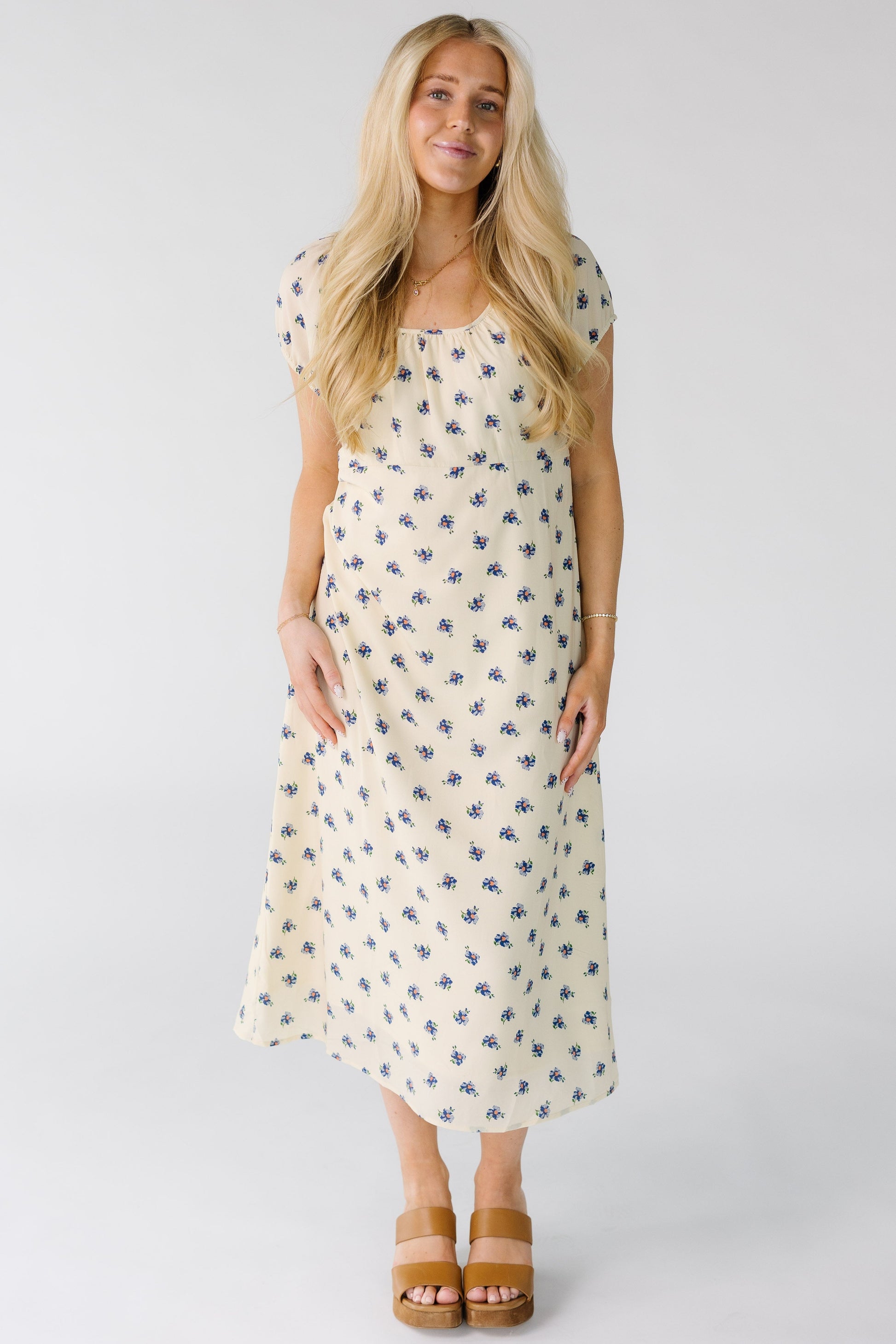 Woman wearing a modest cream and blue floral print midi dress with an empire waist and short puff sleeves.