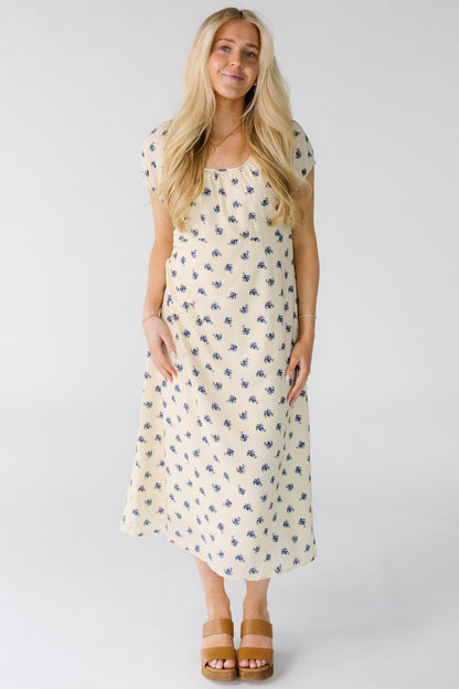 Woman wearing a modest cream and blue floral print midi dress with an empire waist and short puff sleeves.