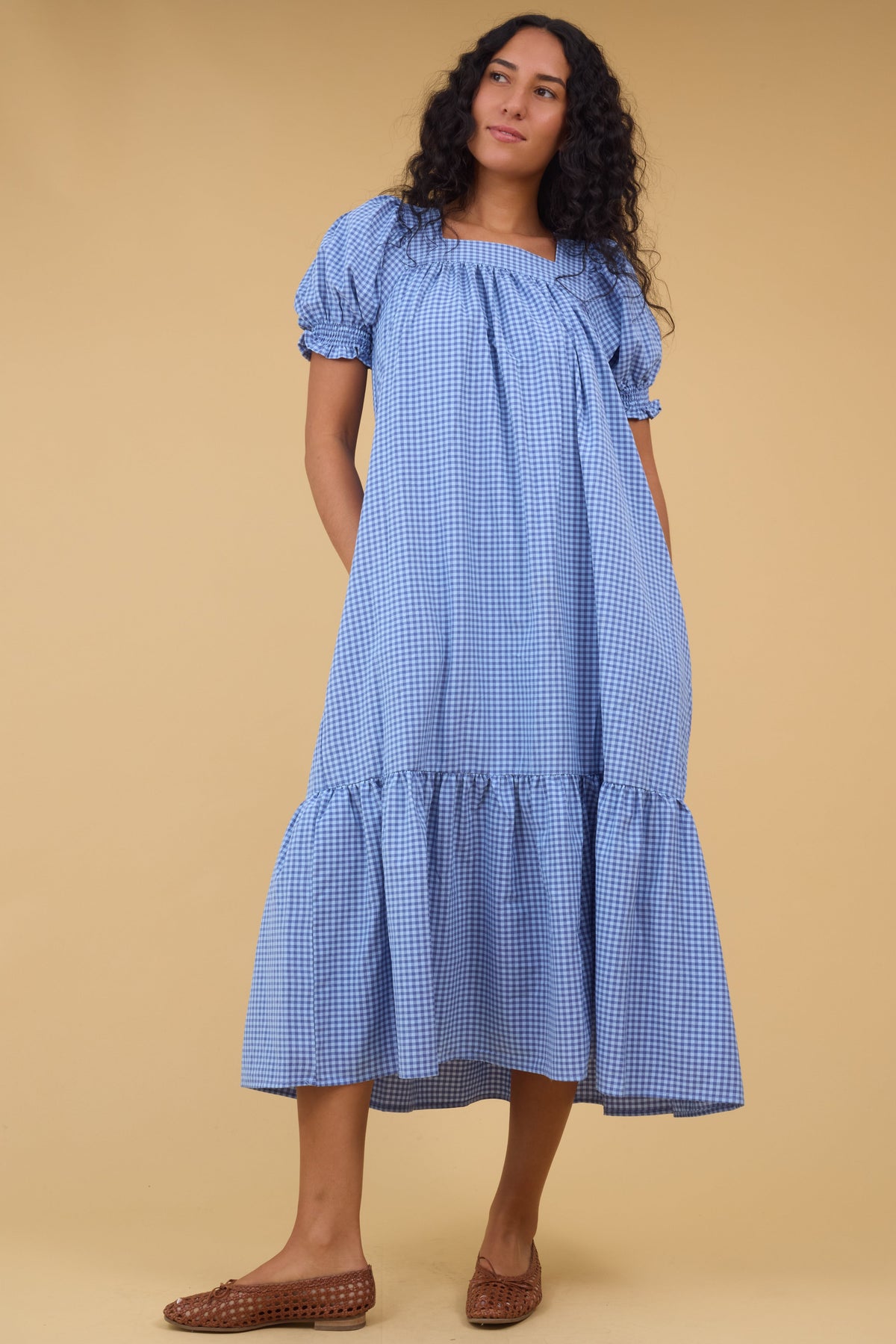 Young woman wearing a modest blue gingham midi dress with a square neckline and a wide bottom ruffle.