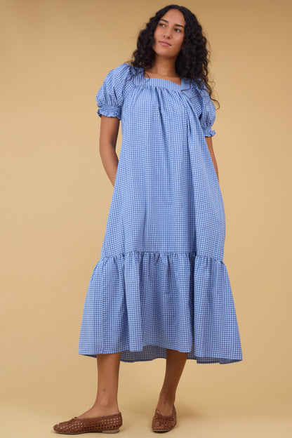 Young woman wearing a modest blue gingham midi dress with a square neckline and a wide bottom ruffle.