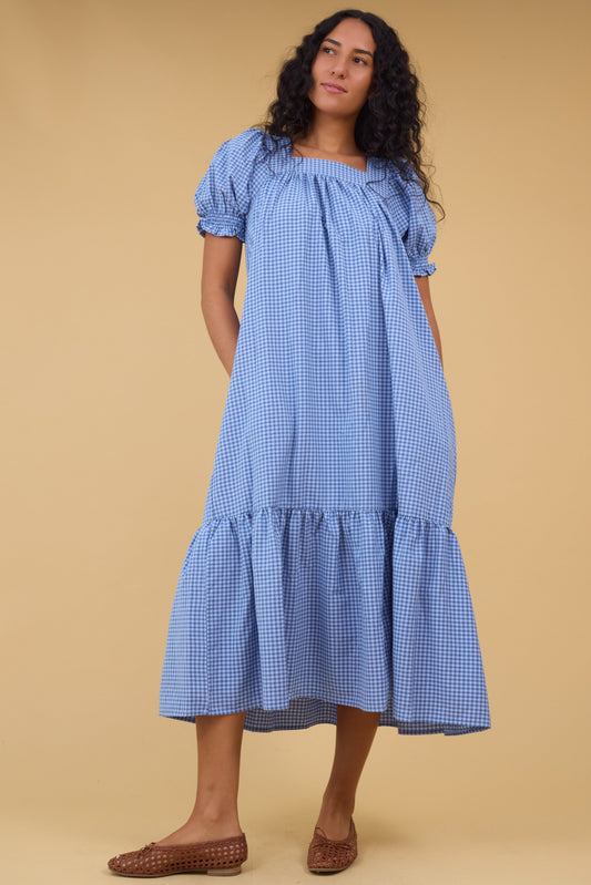 Young woman wearing a modest blue gingham midi dress with a square neckline and a wide bottom ruffle.