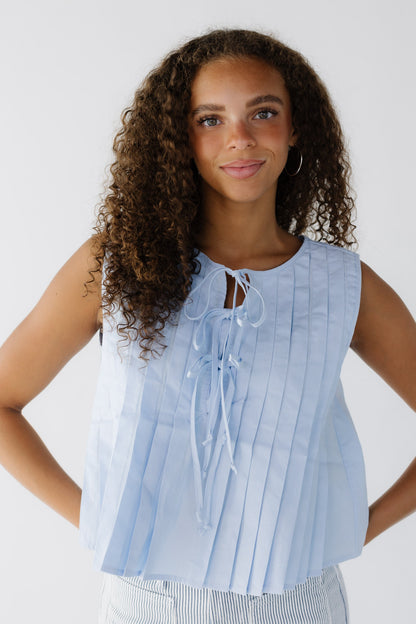 Teenage girl wearing a light blue sleeveless blouse with a round neckline  and pleated front with 3 ties.