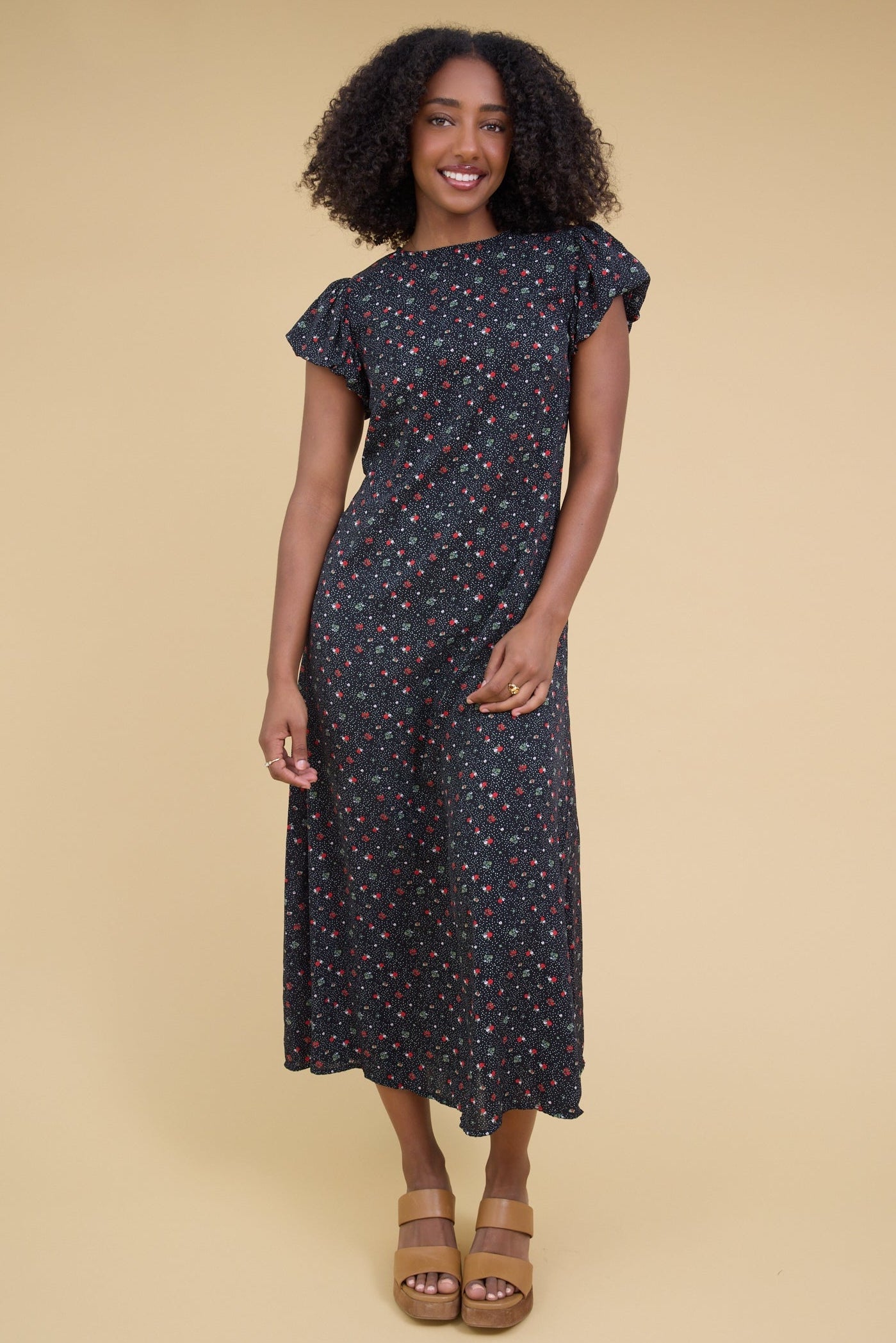 Young girl weairng a black floral print midi dress with short gathered cap sleeves.