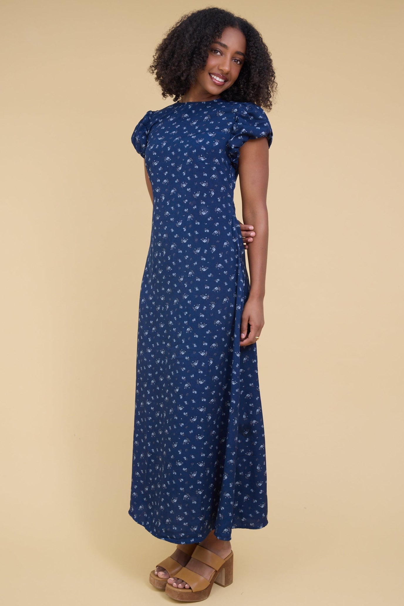 Young woman wearing a modest, close fitting blue floral maxi dress with gathered cap sleeves and a round neckline.