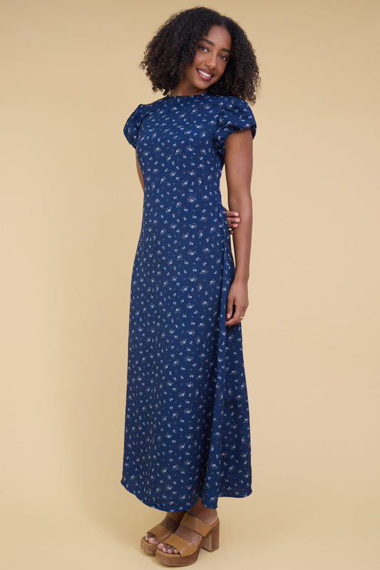 Young woman wearing a modest, close fitting blue floral maxi dress with gathered cap sleeves and a round neckline.