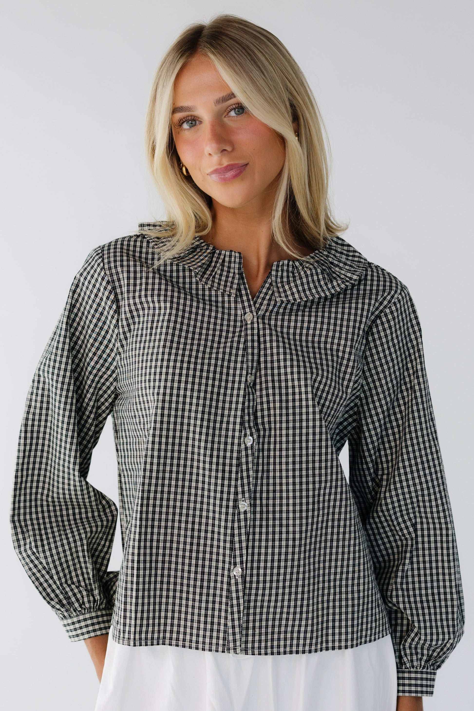 Young woman wearing a black plaid long sleeve blouse with a ruffled collar.