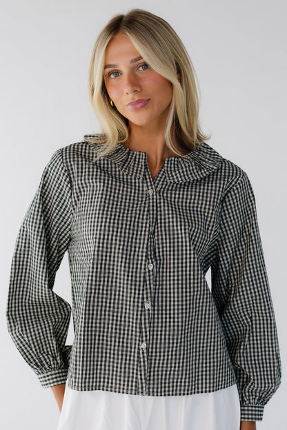 Young woman wearing a black plaid long sleeve blouse with a ruffled collar.