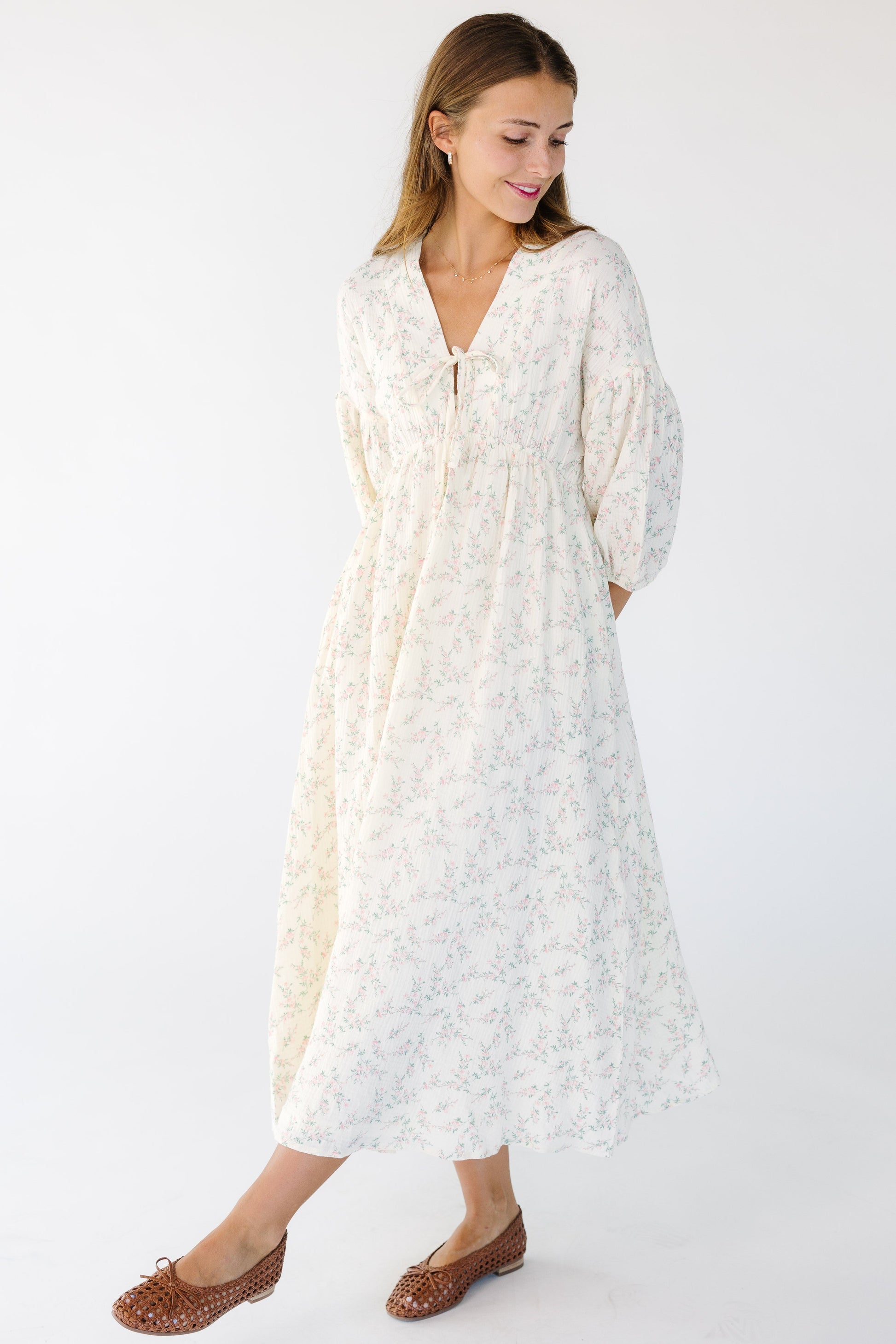 Young woman wearing a modest cream and pink floral midi dress with a V-neckline and half length sleeves.