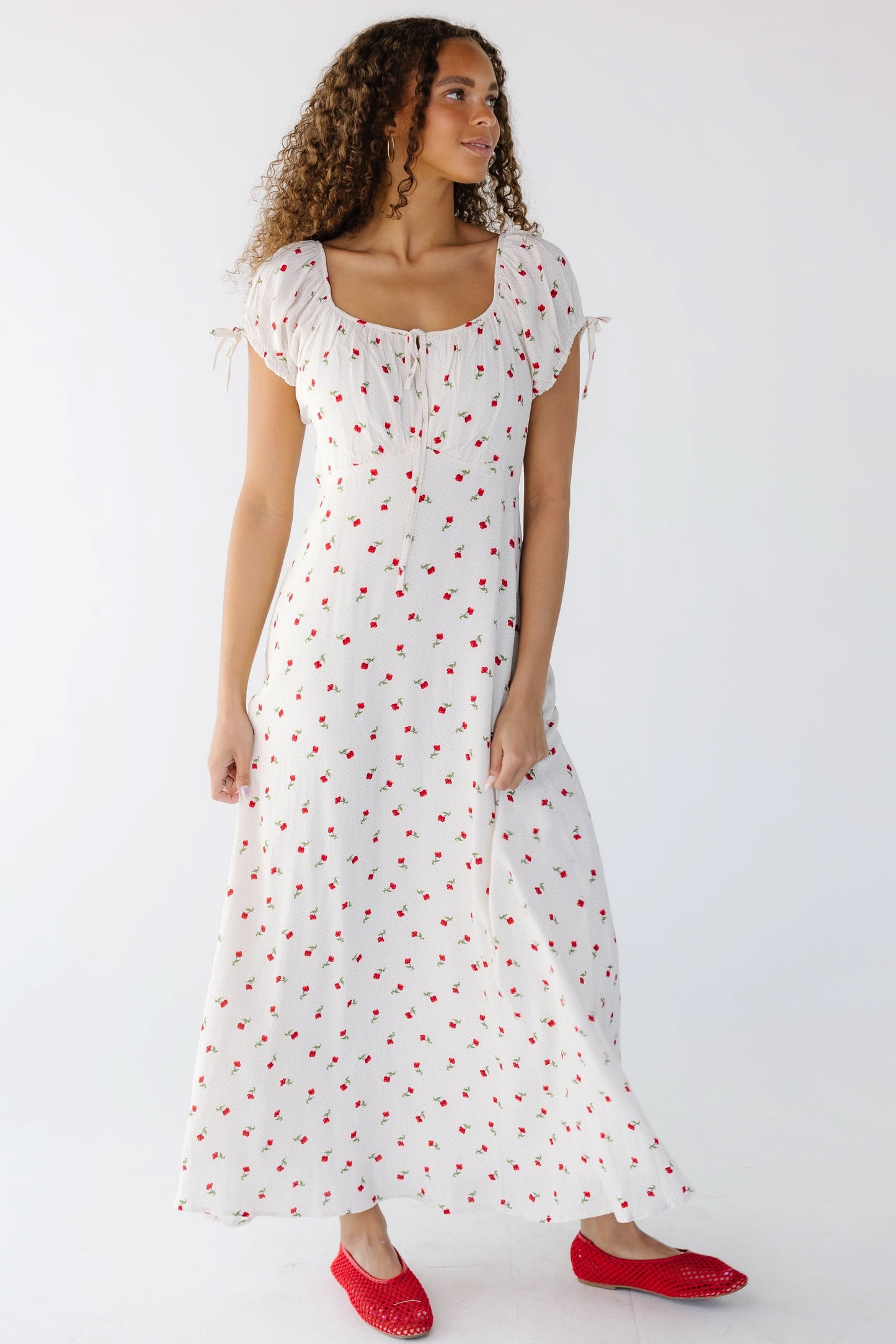 Young woman wearing a  modest white midi-maxi dress with red rose print with short puff sleeves and a wide scoop neckline.