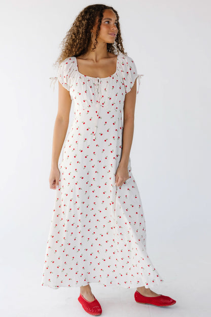 Young woman wearing a  modest white midi-maxi dress with red rose print with short puff sleeves and a wide scoop neckline.