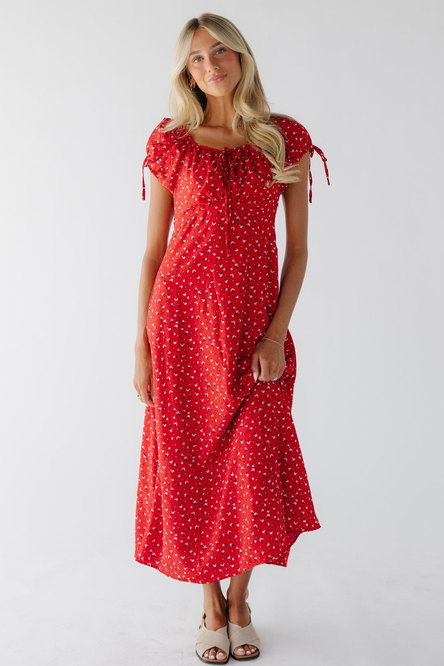 Young woman wearing a red floral midi-maxi dress with an empire waist, short puff sleeves and a drawstring scoop neckline.
