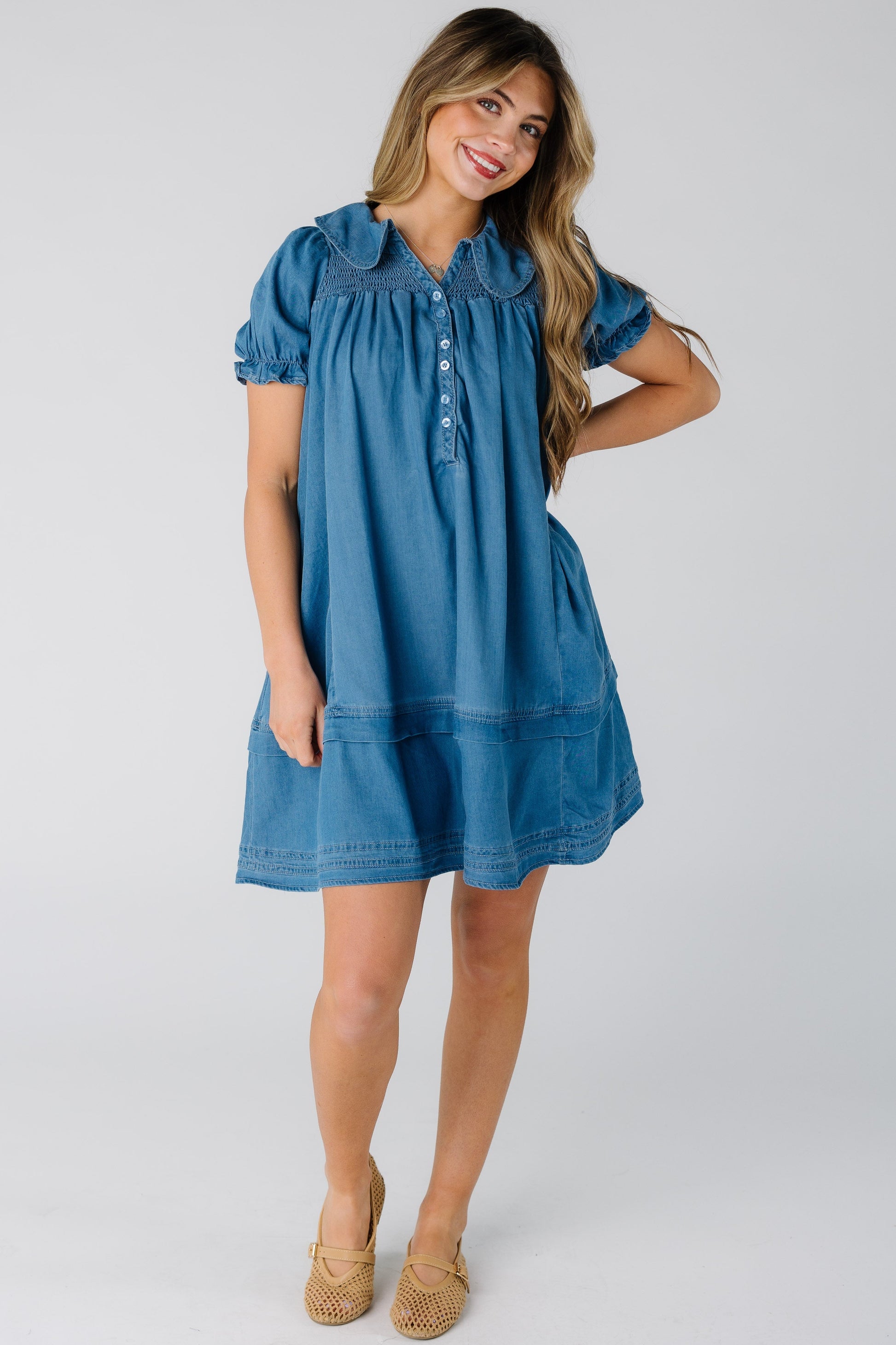 Woman wearing a knee length denim dress with short puff sleeves and rounded point collar.