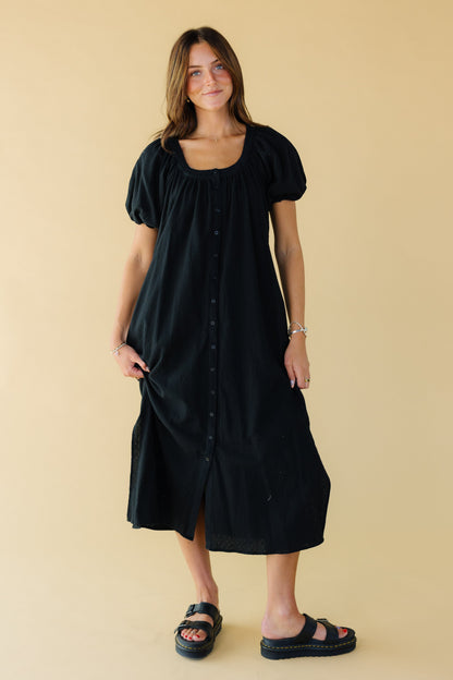 Young woman wearing a modest black button down midi dress with balloon sleeves and a scoop neckline.