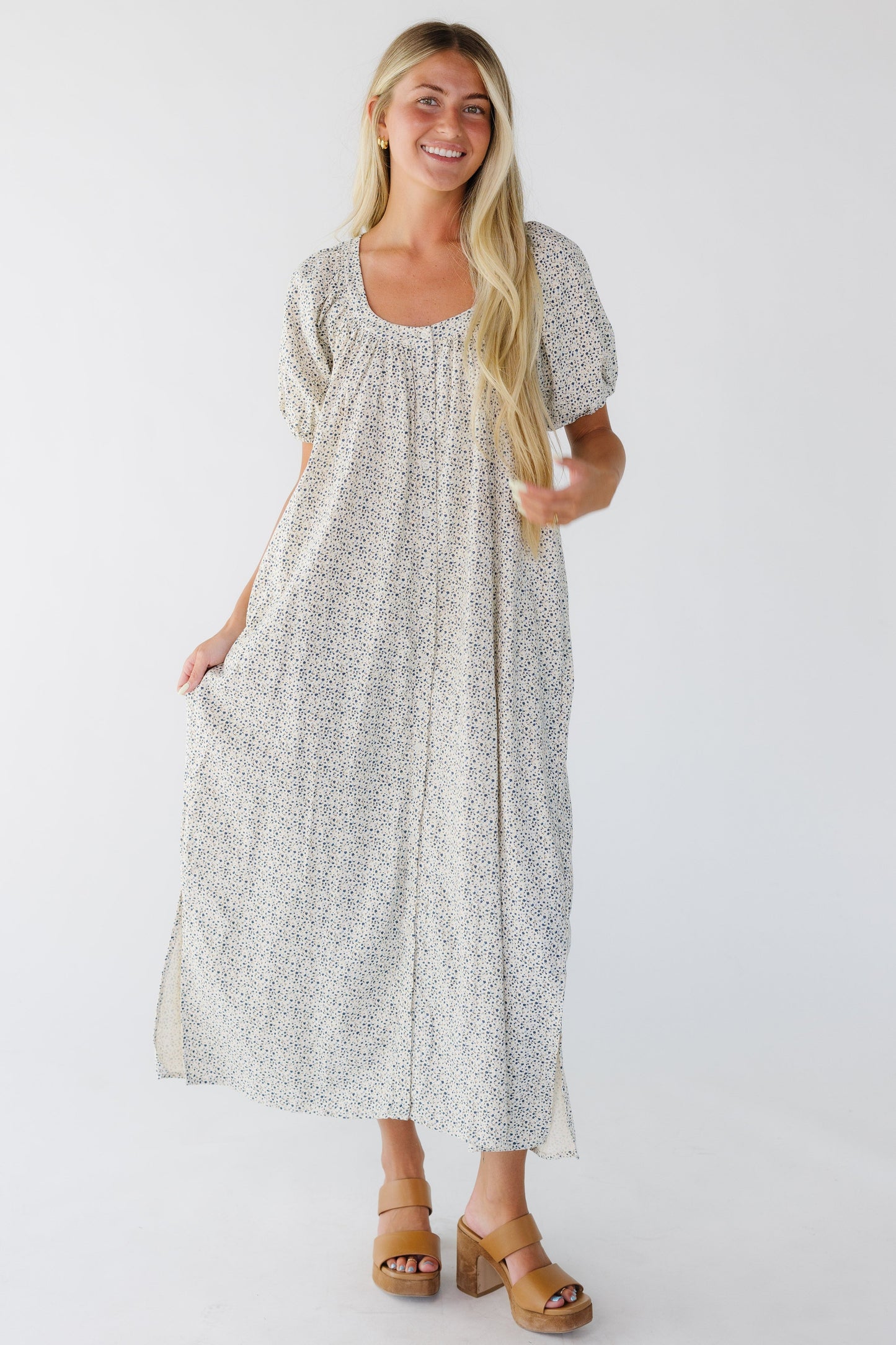 Young woman wearing a cream & blue floral midi-maxi button down dress with a scoop neckline and balloon sleeves.