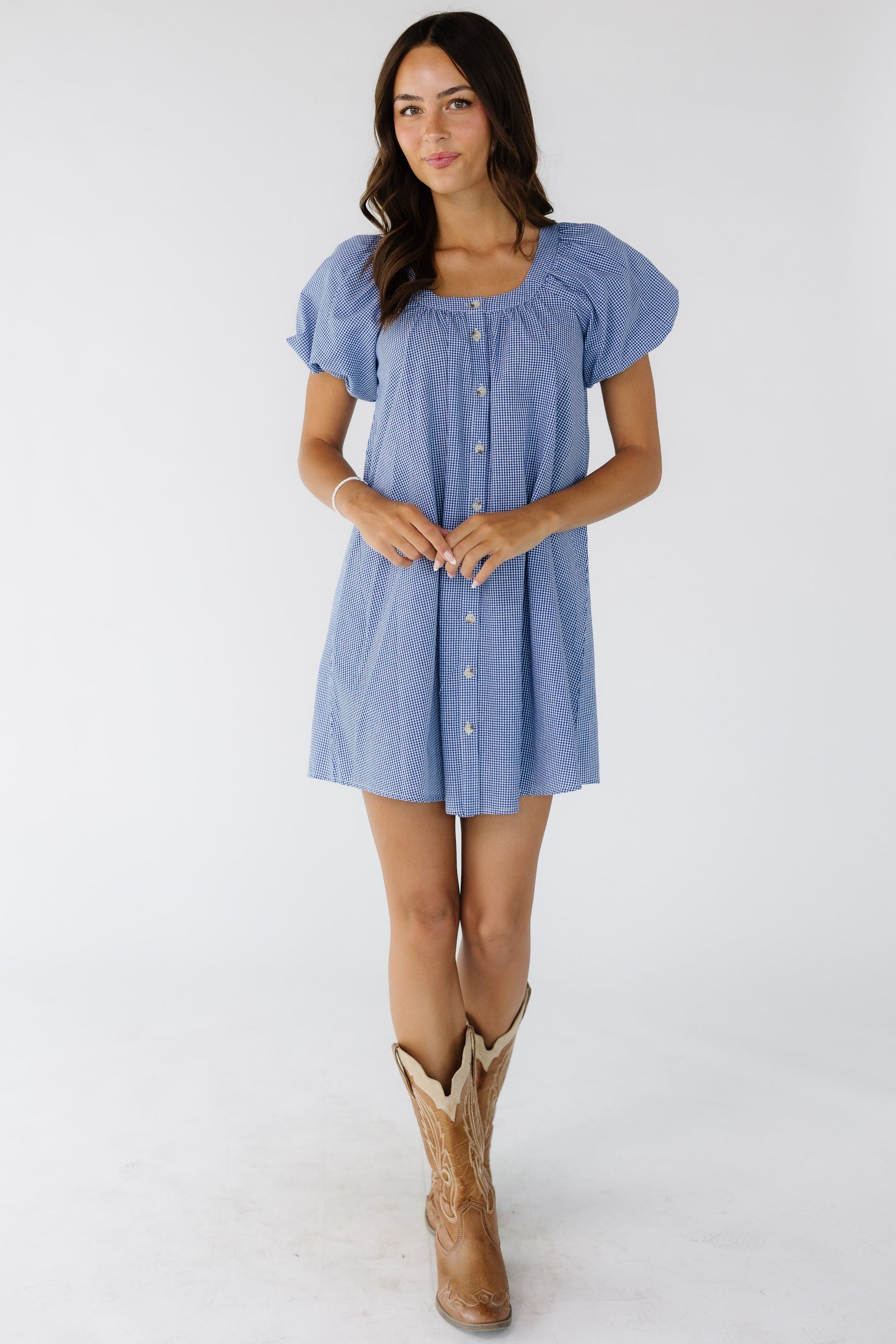 Young woman wearing a navy & white gingham, button down short dress with a scoop neckline and balloon sleeves.