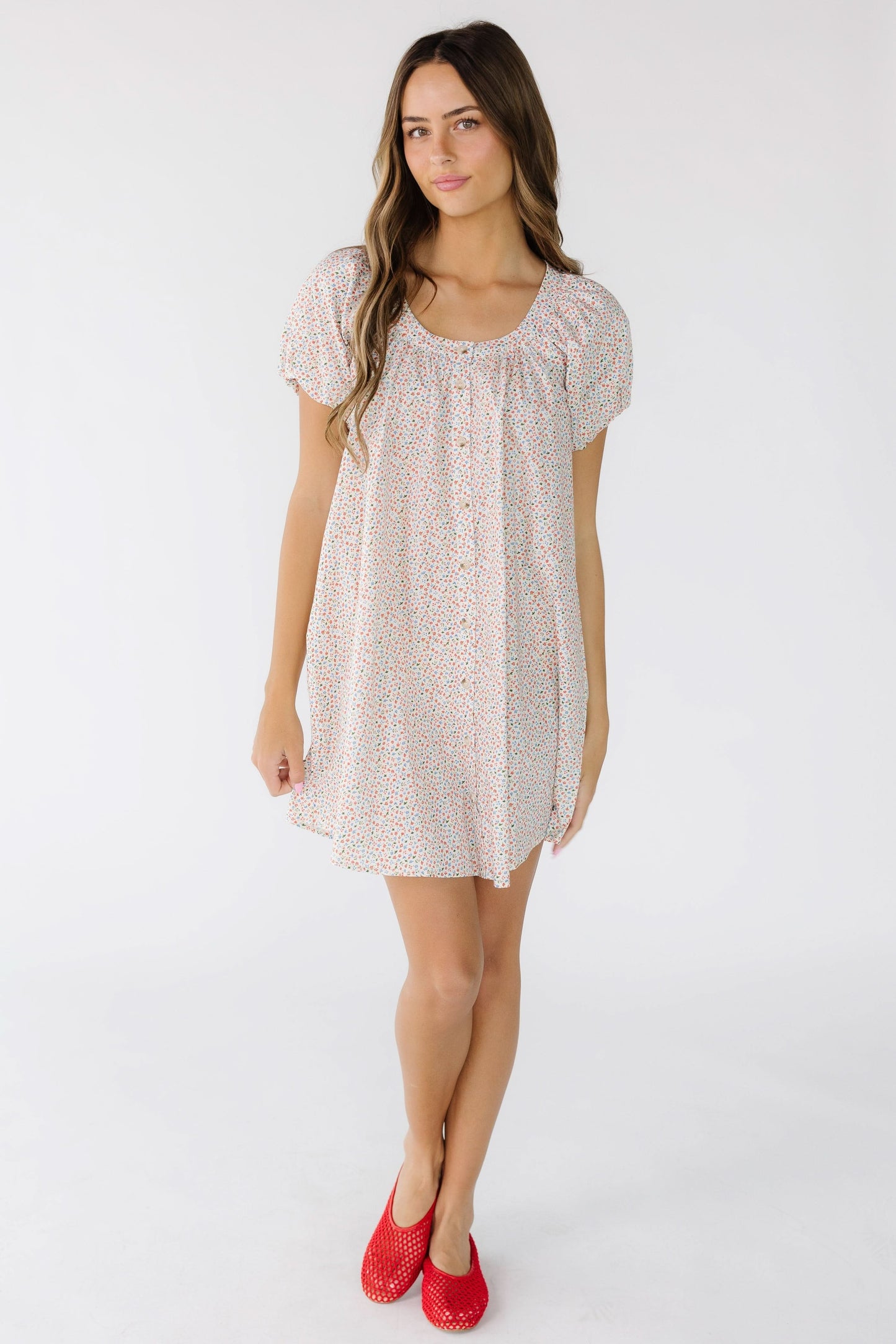 Young woman wearing a white floral print short dress with a Scoop neckline and short puff sleeves cut above the knee.