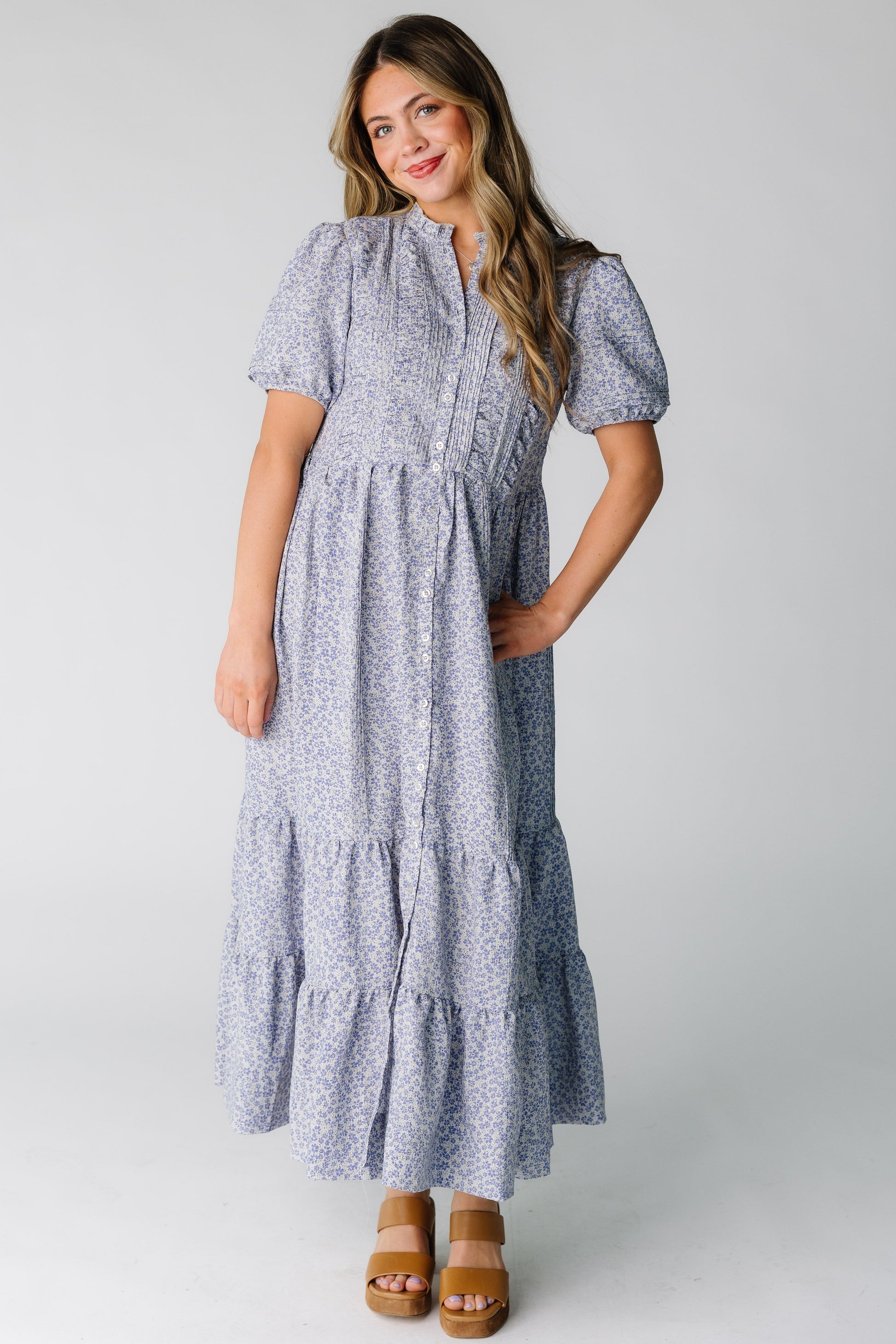 Woman wearing a purple floral print tiered midi dress in button down style and short sleeves.