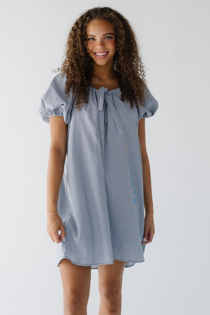 Young woman wearing a navy & white gingham short dress with balloon sleeves and a drawstring and scoop neckline.
