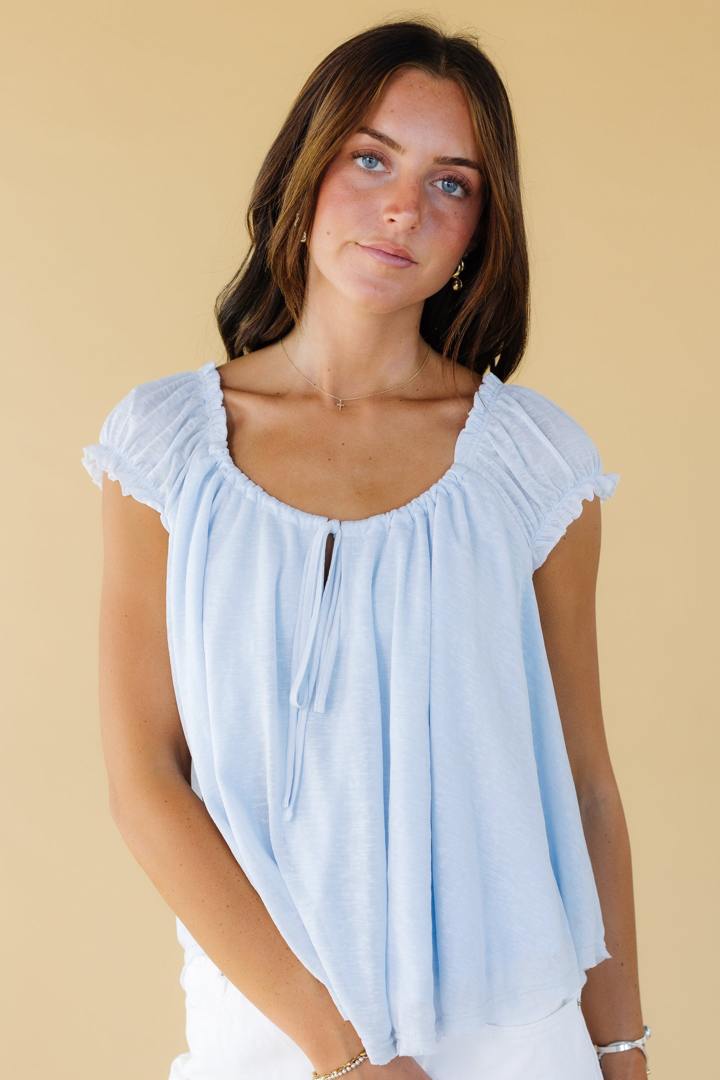 Young woman wearing a light blue very loose fitting blouse with short gathered cap sleeves and a scoop neckline.