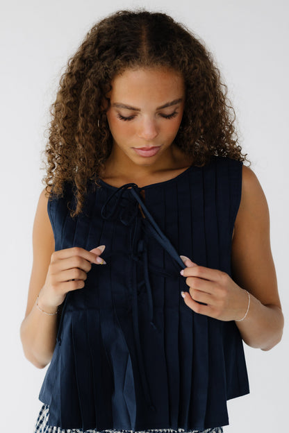 Teen girl wearing a sleeveless navy pleated blouse with 3 front tie clousre.