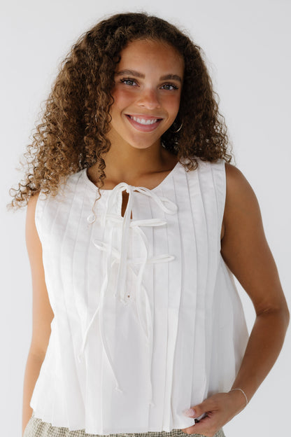 Teen girl wearing a white sleeveless pleated blouse with 3 front tie closure.