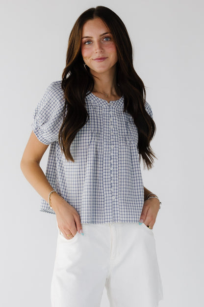 Young woman wearing a modest white and blue plaid button down loose fitting blouse with puff sleeves and a round neckline.