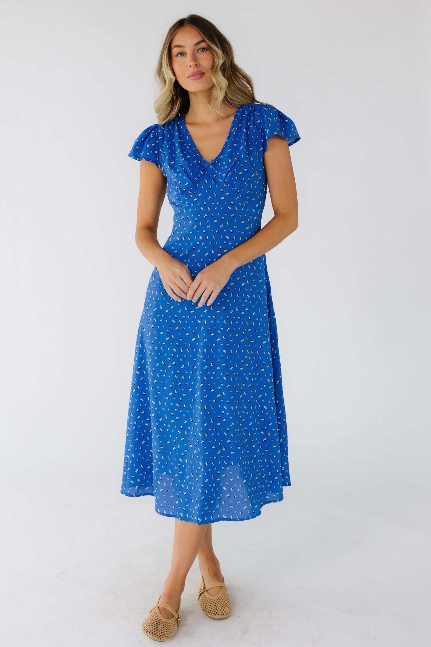 Young woman wearing a blue print midi dress with flutter sleeves, V-neckline and a pointed empire waist.