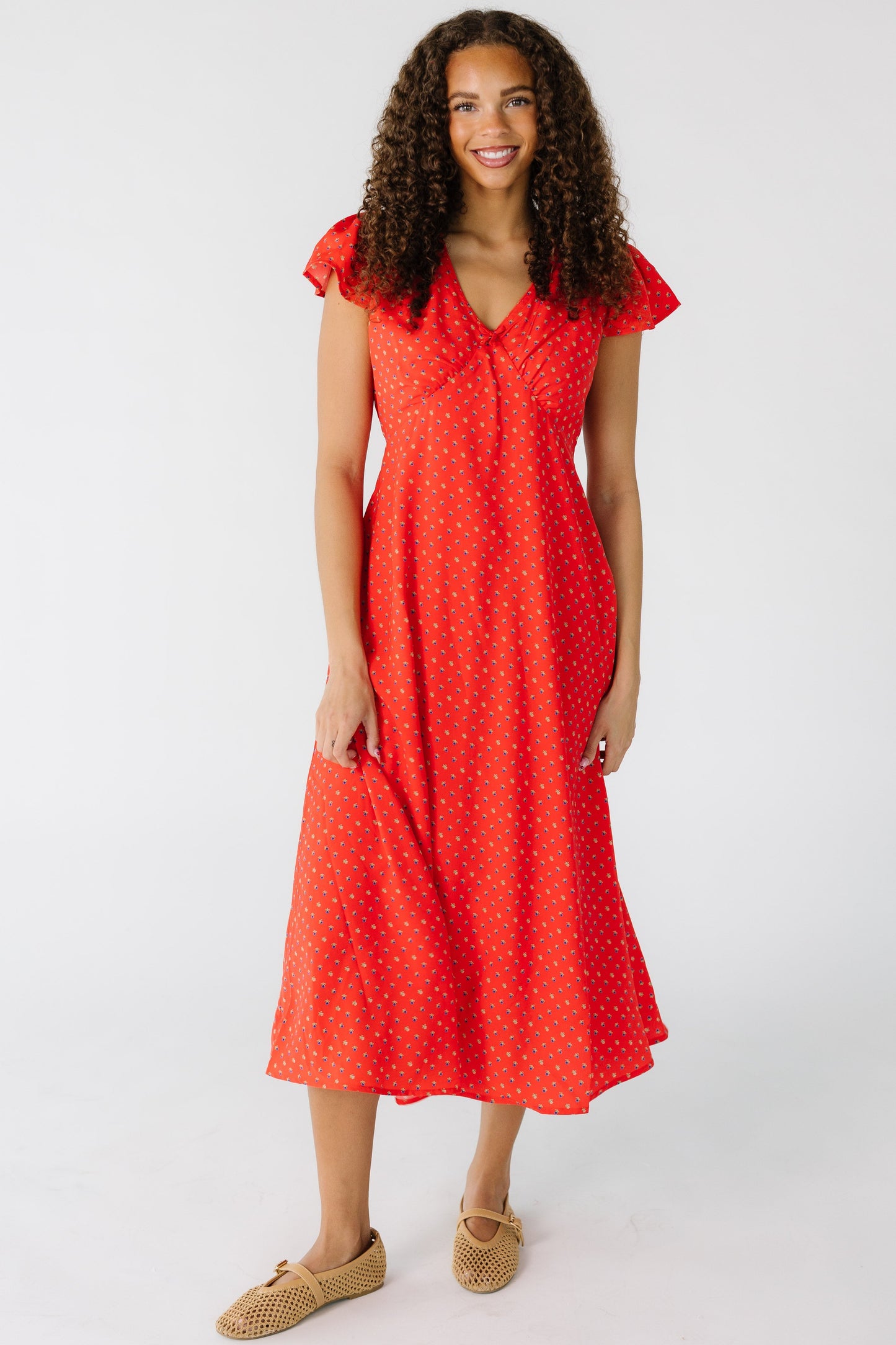 Teen girl wearing a modest red print midi dress with a V-neckline and short flutter sleeves.