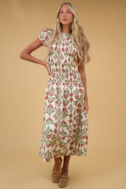 Young woman wearing a modest cream floral midi dress with shrot puff sleeves and a smocked bodice down to a drop waist with full skirt.