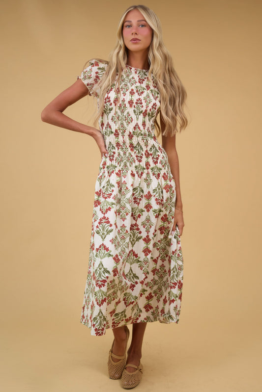 Young woman wearing a modest cream floral midi dress with shrot puff sleeves and a smocked bodice down to a drop waist with full skirt.