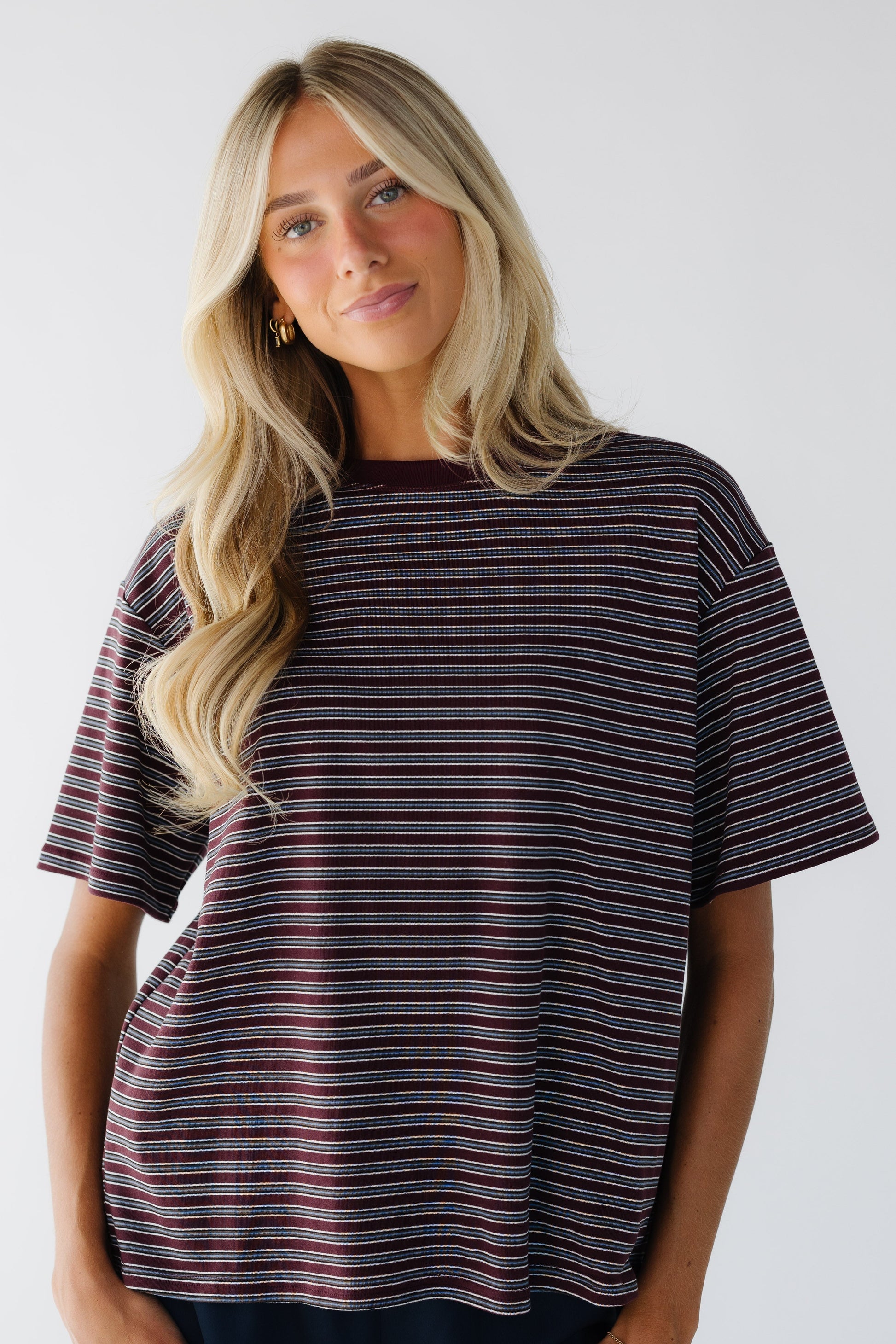 Young woman wearing a burgundy & grey stripe loose fitting tee with short sleeves and a crew neckline.