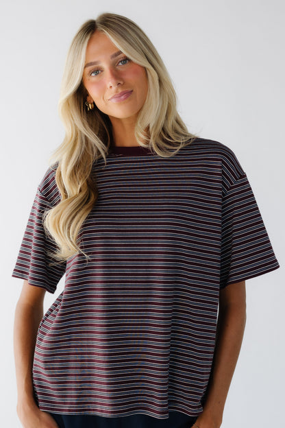 Young woman wearing a burgundy & grey stripe loose fitting tee with short sleeves and a crew neckline.