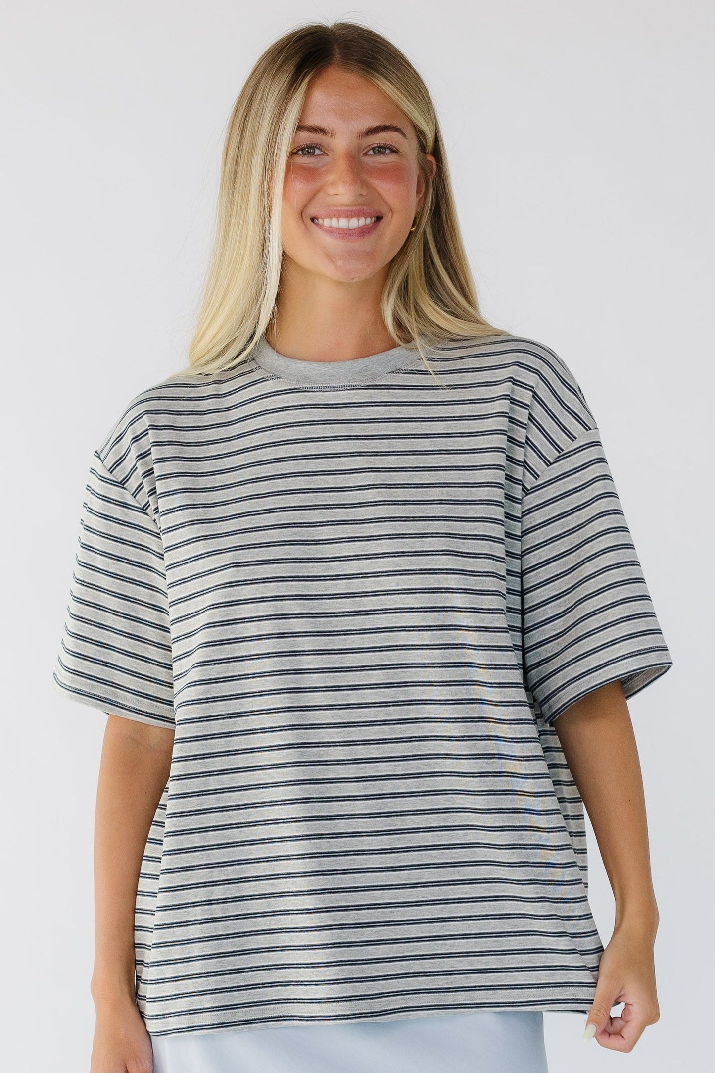 Young woman wearing a grey stripe loose fitting tee with short sleeves and a crew neckline.