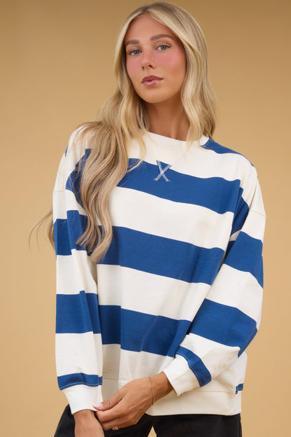 Young woman wearing a modest ivory & blue, wide stripe oversized top with long sleeves.