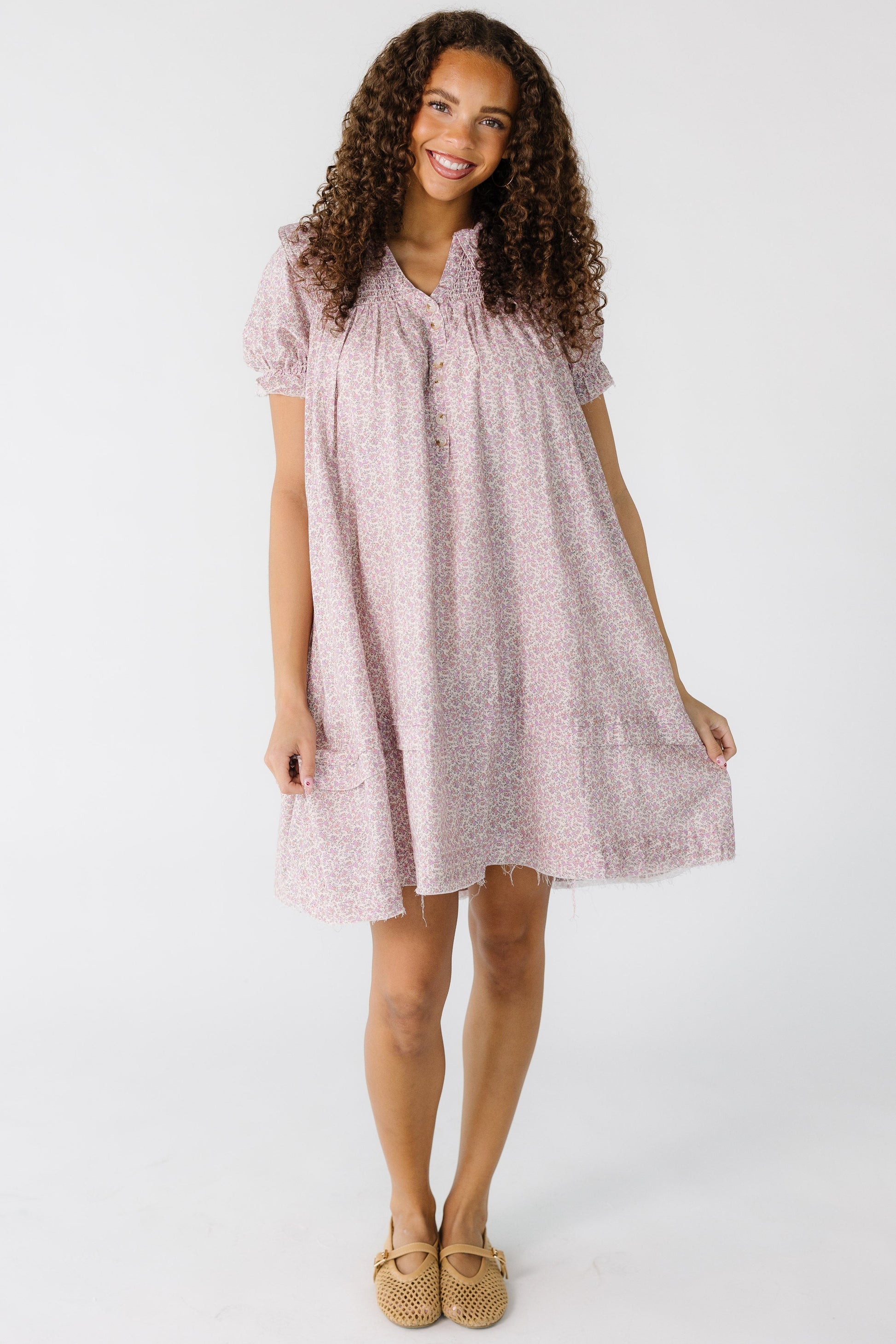 Teenage girl wearing a pink floral dress cut above the knee with short sleeves.