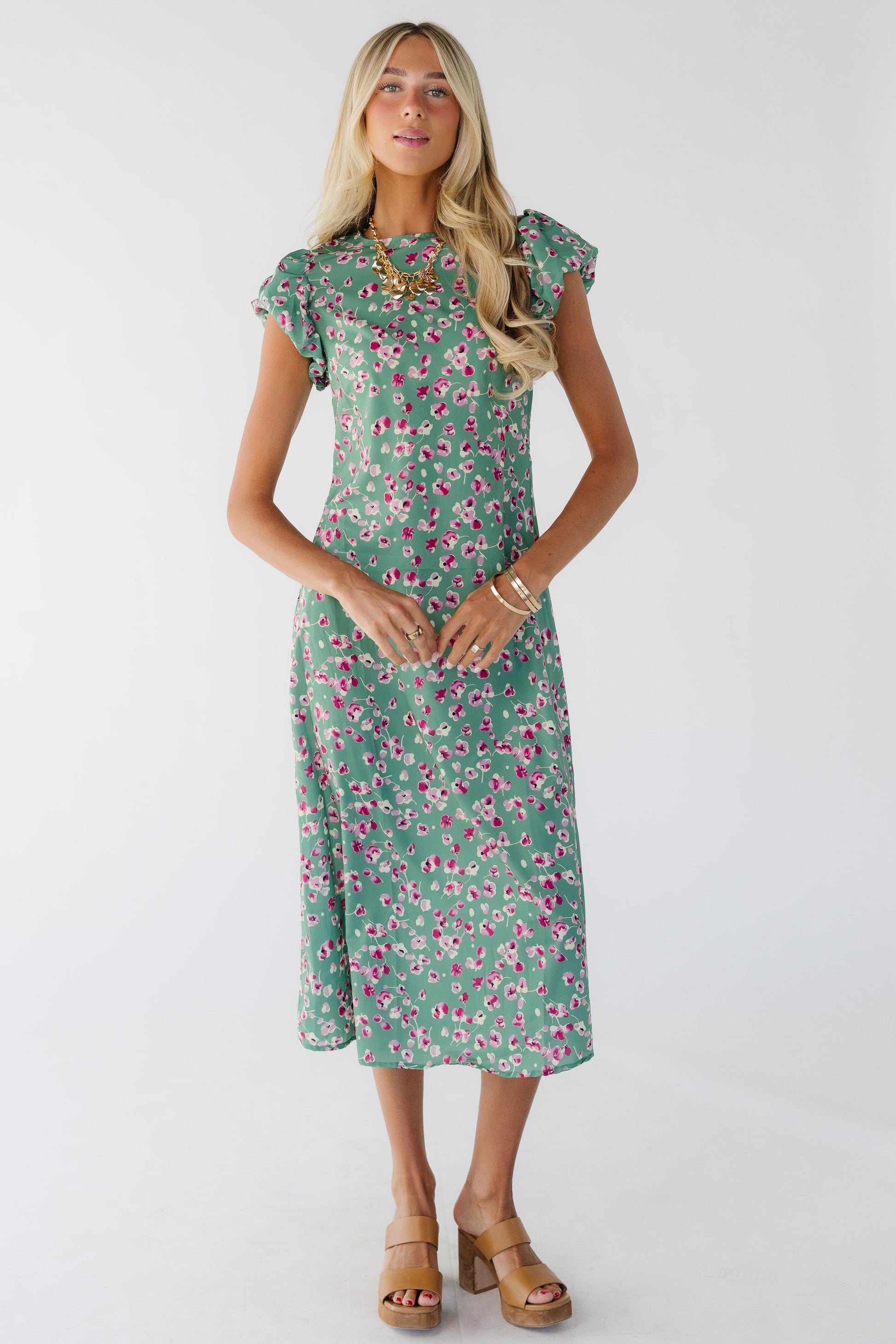 Woman wearing a green floral midi dress with a round neckline and puff-cap sleeves.