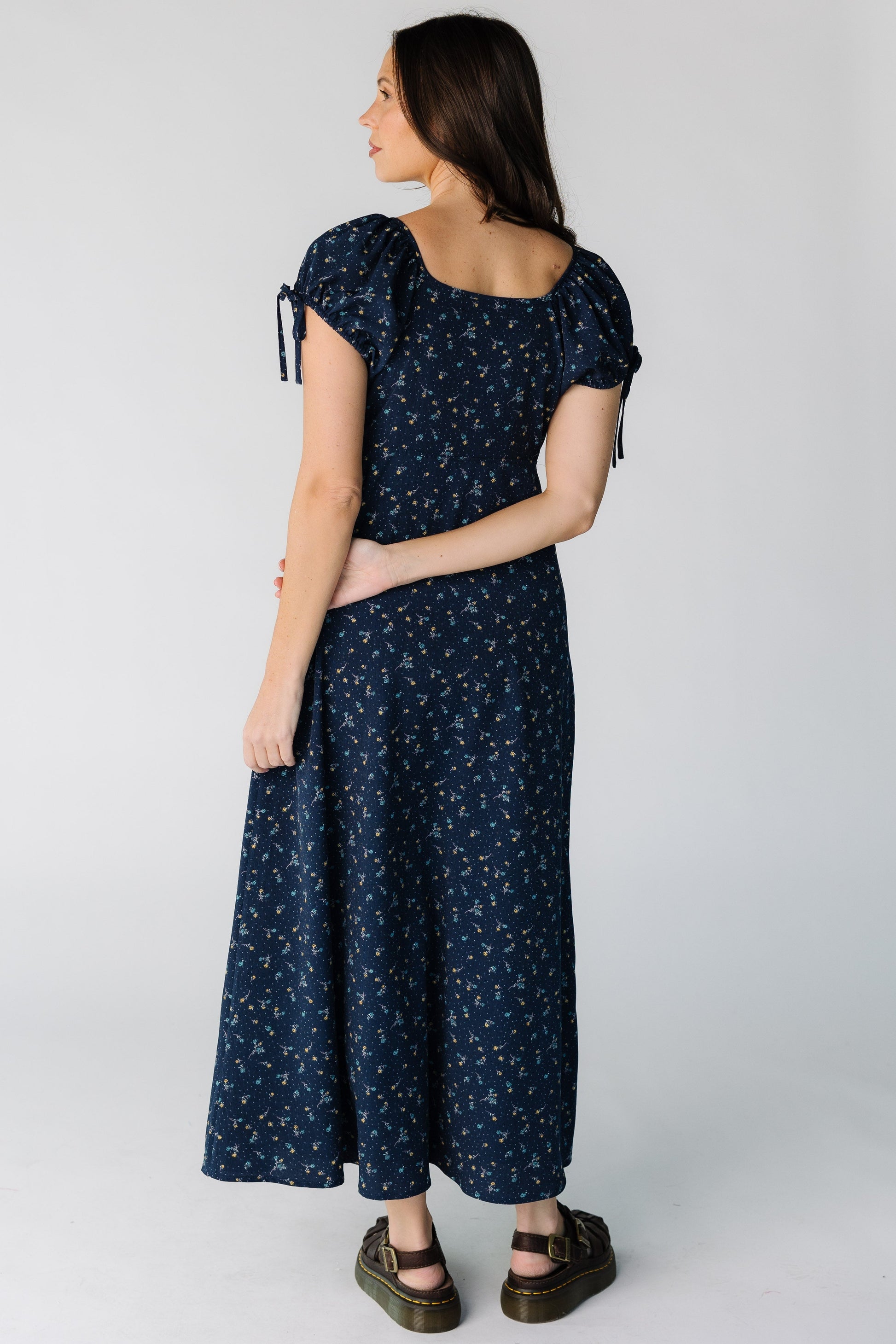 Back view of a woman wearing a navy floral print midi dress with a square neckline and short puff sleeves.