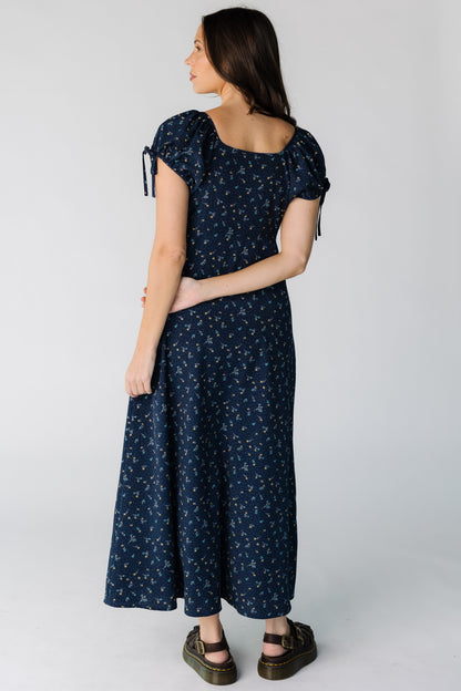 Back view of a woman wearing a navy floral print midi dress with a square neckline and short puff sleeves.