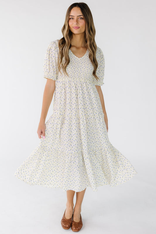 Young woman wearing an ivory floral print midi dress with a V-neckline, Smocked front and back bodice, and multiple gathered tiers.