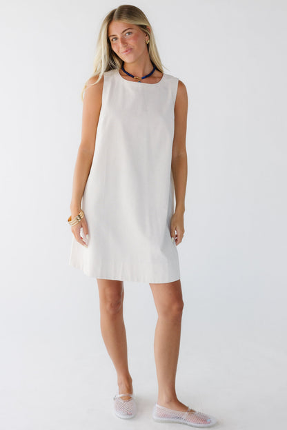 Young woman wearing a cream sleeveless shift dress.