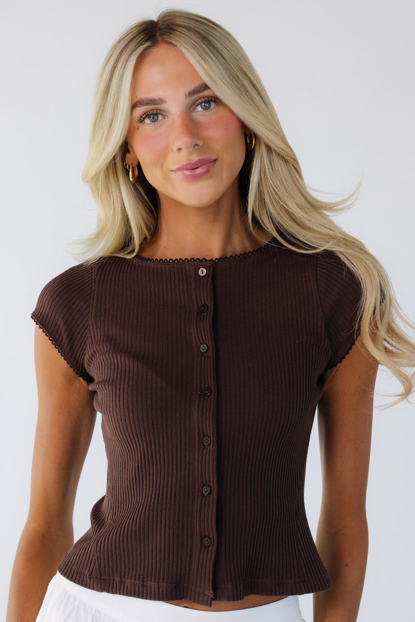 Young woman wearing a snug, modest button down top in rib knit with a round neckline and cap sleeves.