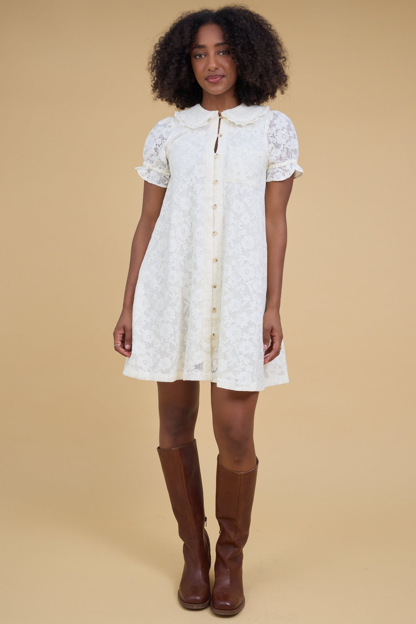 Young woman wearing an off white all lace short dress that buttons down the front with elastic loop button holes and short sleeves.