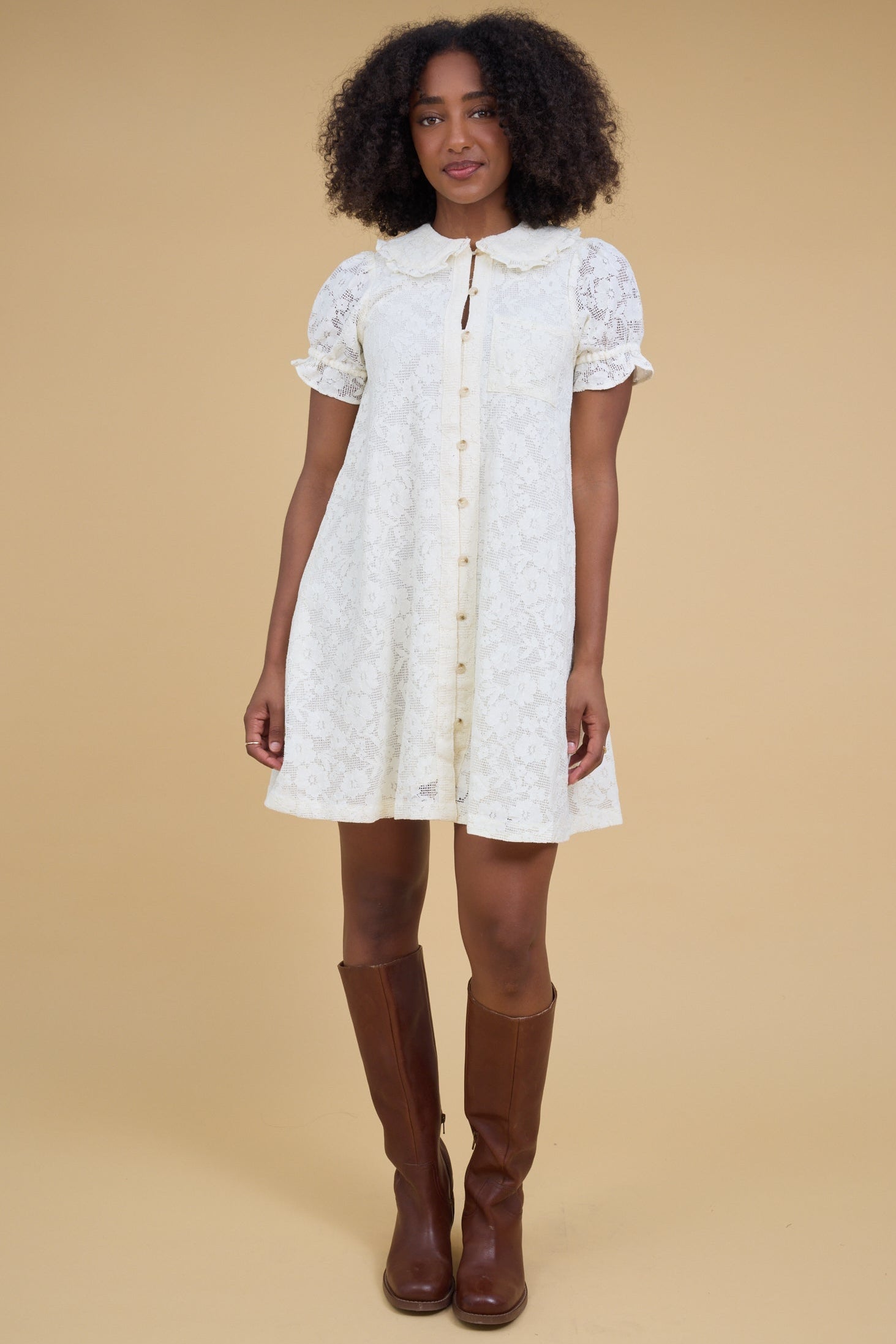 Young woman wearing an off white all lace short dress that buttons down the front with elastic loop button holes and short sleeves.