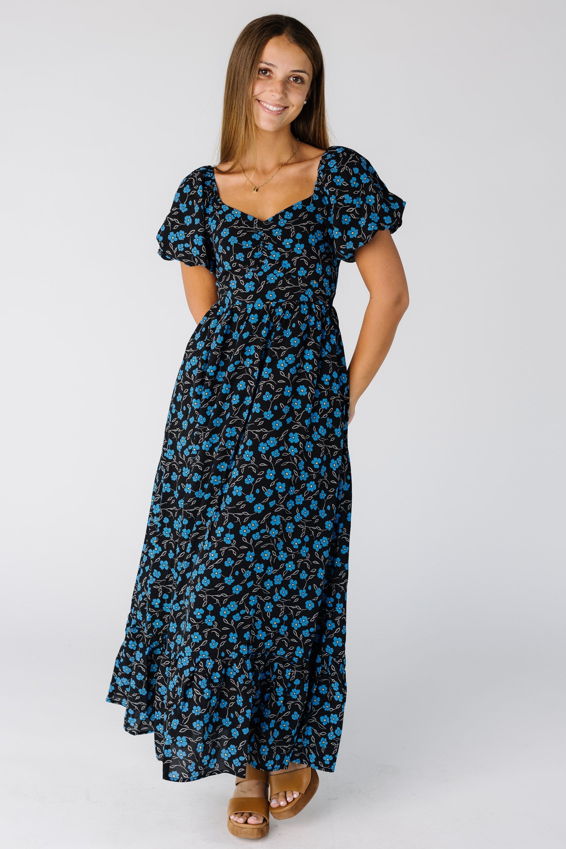 Woman wearing a  midi/maxi dress in blue floral print with a close fitting bodice and full midi skirt