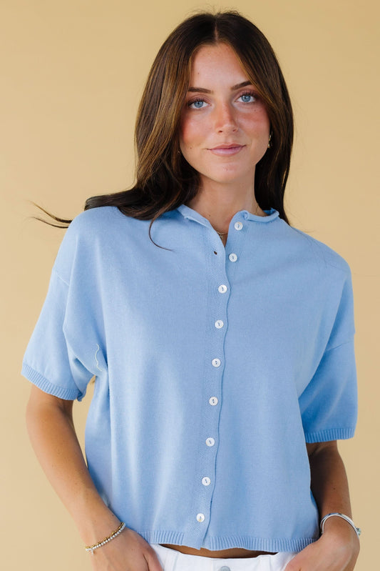 Young woman wearing a modest light blue button down cardigan with short sleeves and a round rolled neckline.